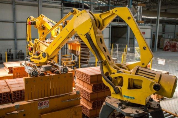 Großes Industrie-Lager mit gestapelten Kisten, Kranen, Zaun, Pfählen und einer fernen Wand in einer automatisierten Fertigungsanlage.