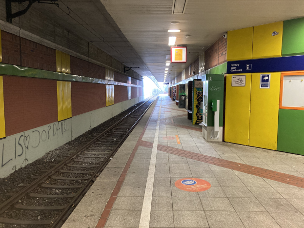 Ein Bahnsteig in Berlin Hauptbahnhof, Deutschland, mit einem stehenden Zug auf den Gleisen, Deckenleuchten, die den Bereich beleuchten, Graffiti an einer linken Wand und ein paar Gegenständen auf der rechten Seite.