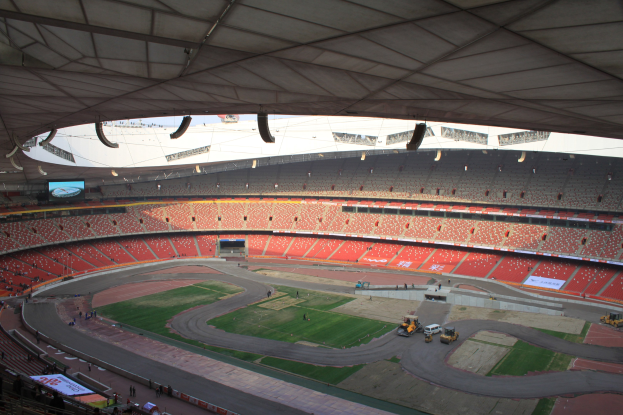 Großes Stadion voller Zuschauer, Fahrzeuge auf der Straße, Rasen, Texttafeln, Geländer und Deckenbeleuchtung mit einem Bildschirm.