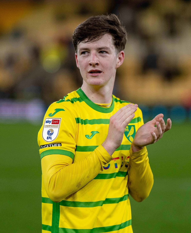 Ein junger Mann in einem gelben und grünen T-Shirt klatscht auf einem Fußballfeld, feiert ein Tor mit einem unscharfen Hintergrund.