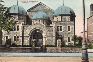 Eine alte Ansichtskarte zeigt die jüdische Synagoge in Cardiff, Ontario, Kanada, mit einem Gebäude mit Fenstern, Türen und Bögen, umgeben von Pflanzen, einem Zaun, Bäumen, einem Pfahl und einem bewölkten Himmel, mit Text oben.