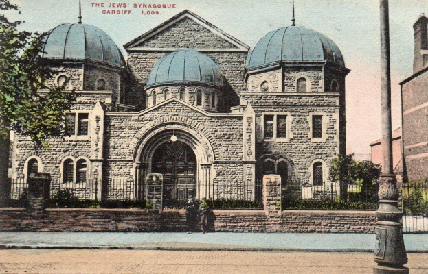 Eine alte Ansichtskarte zeigt die jüdische Synagoge in Cardiff, Ontario, Kanada, mit einem Gebäude mit Fenstern, Türen und Bögen, umgeben von Pflanzen, einem Zaun, Bäumen, einem Pfahl und einem bewölkten Himmel, mit Text oben.