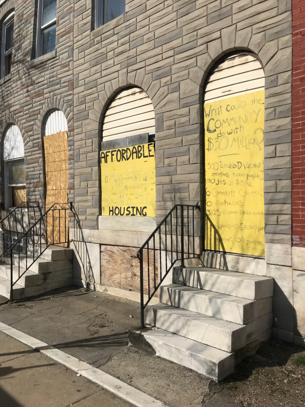 Ein verbarrikadiertes Gebäude mit einer Tafel, die "Bezahlbarer Wohnraum" lautet, eine Treppe mit Geländer, die zum Eingang führt, und eine Straße unten.