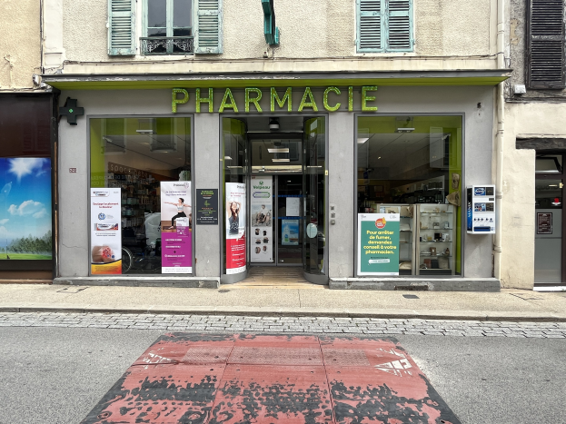 Apotheke mit Glaswänden und -türen, Plakate an den Innenwänden, an einer Straßenecke gelegen mit einer Straße unten.