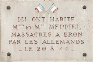 Ein Steintafel an einem Gebäude mit zwei Flaggen, beschriftet mit Text, der ein Massaker gedenkt.