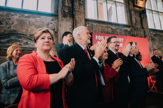 Eine Gruppe von Menschen, die vor einem Publikum jubeln und ein Banner mit der Aufschrift "Wahlsieg" hinter sich haben.