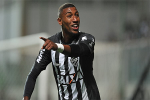 Fußballspieler in schwarzer und weißer gestreifter Jerseys, der grinsend und ein Tor feiernd, mit einem unscharfen Hintergrund.