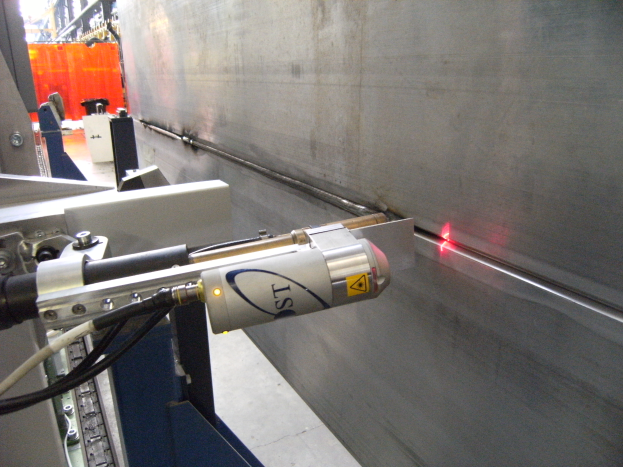 Eine Laserschneidmaschine in einer Fabrik strahlt helles Licht aus und erleuchtet die Umgebung mit einer Wand auf der rechten Seite und einigen Gegenständen im Hintergrund.