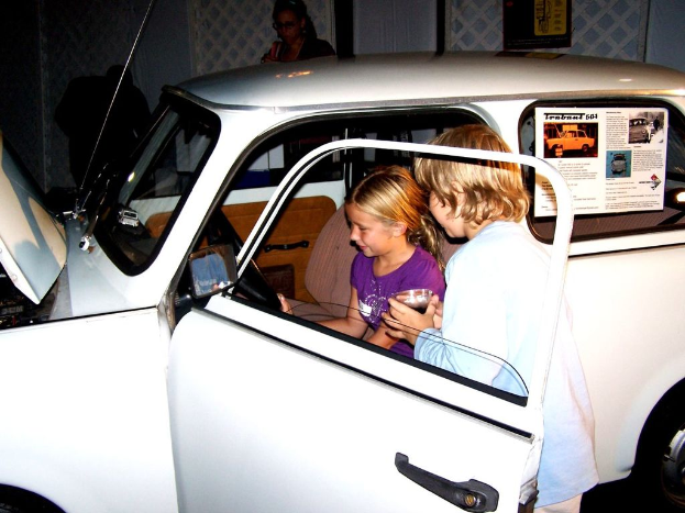 Zwei Kinder versuchen, in ein Auto mit anderen Personen im Hintergrund zu steigen.