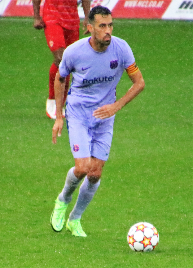 Ein Fussballspieler in einem Sportoutfit und -schuhen ist im Einsatz auf dem Feld, mit einer Tafel mit Text im Hintergrund.