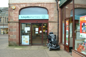 Apothekenladen mit einem vor dem Gebäude geparkten Fahrzeug und einem Gebäude in der linken Ecke.