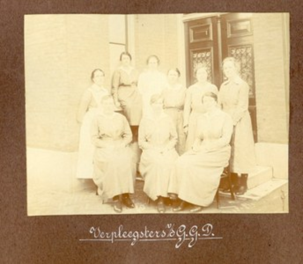 Schwarzes und weißes Foto einer Gruppe von Frauen, die auf den Stufen eines Gebäudes sitzen, mit einer Wand und einer Tür im Hintergrund und Text unten.