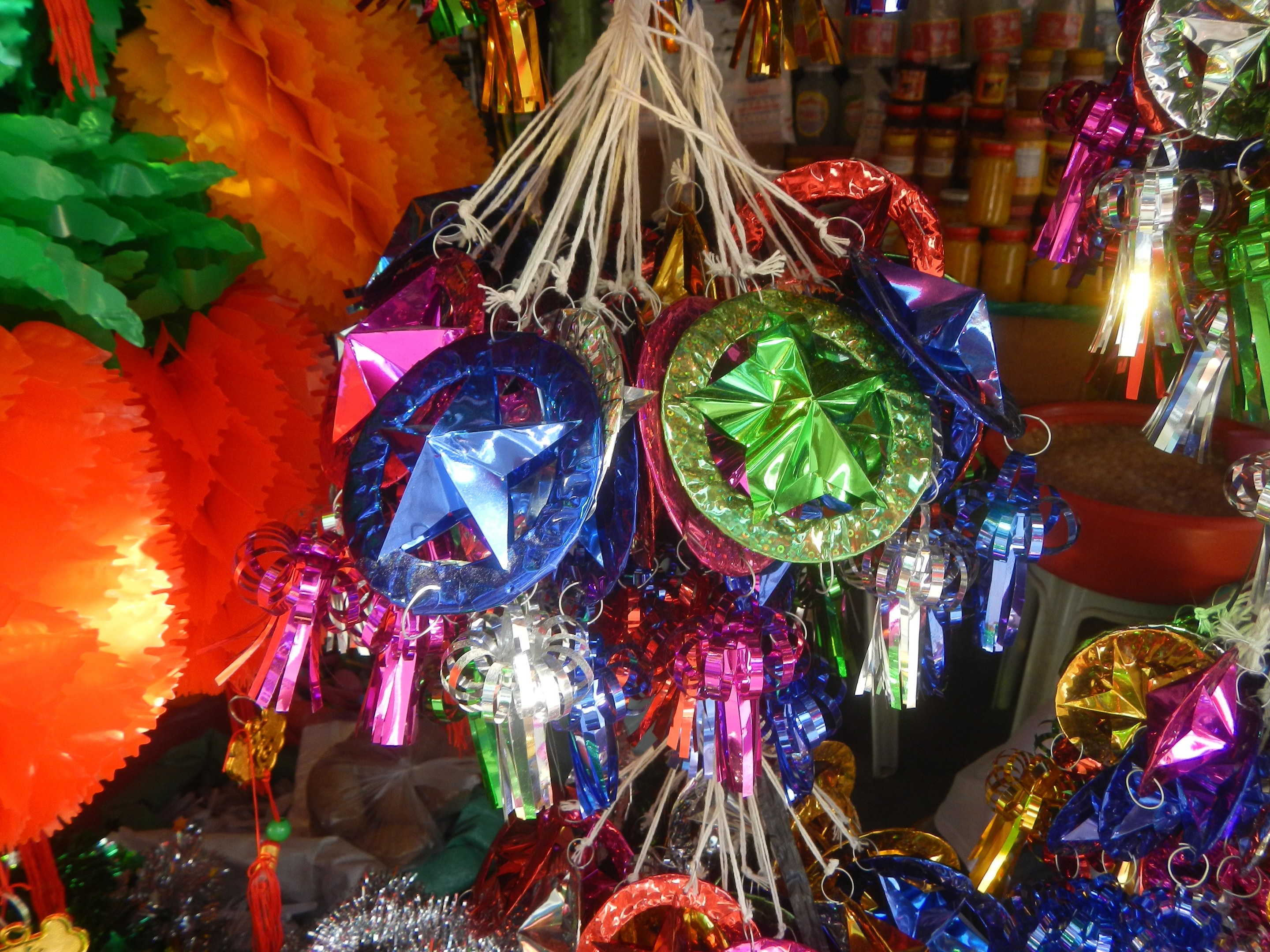 Farbenfrohe Dekorationen wie Laternen und Bänder hängen von der Decke über Regalen mit Flaschen in einer festlichen Atmosphäre.