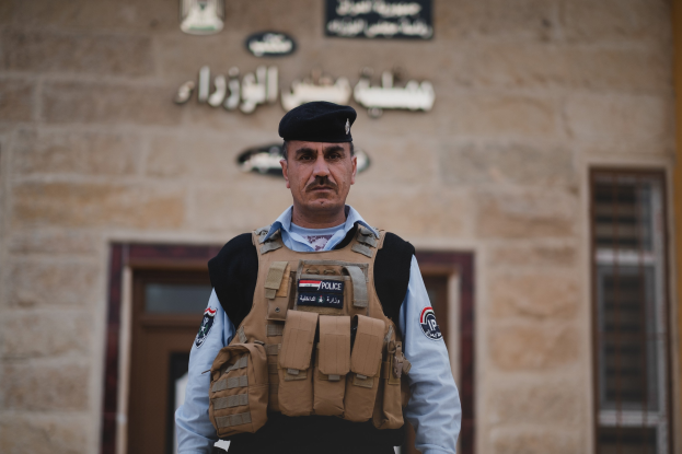 Polizist in Uniform vor einem Gebäude mit Türen, Fenstern und Text an der Wand stehend.