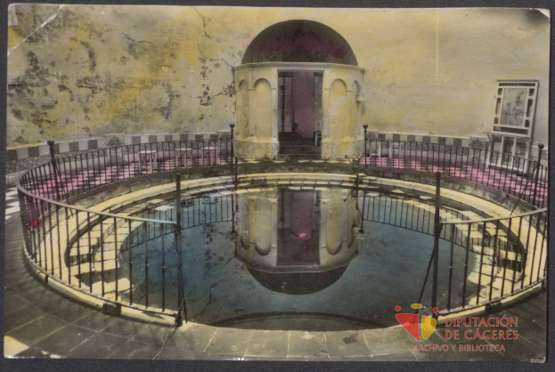 Altes Schwarz-Weiß-Foto eines Gebäudes mit einem zentralen Pool, der von einem Geländer und einer Wand umgeben ist; Text und ein Logo sind unten zu sehen.