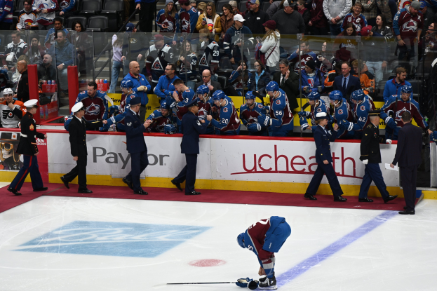 Eishockeyspieler auf dem Eis umgeben von Teamkollegen und Gegenspielern, mit Zuschauern im Hintergrund bei einem NHL-Spiel zwischen Colorado Avalanche und San Jose Sharks am 24. März 2015.