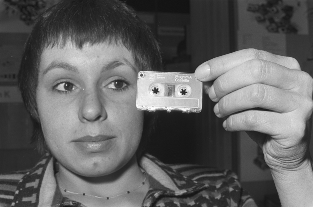 Eine Frau hält eine Kassette vor ihrem Gesicht an einer Wand, dargestellt in Schwarz-Weiß.