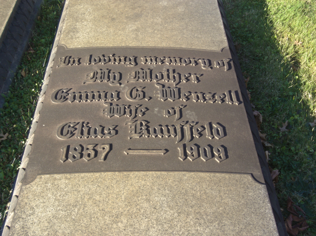 Grabstein auf einem Friedhof mit der Inschrift "In liebevoller Erinnerung an meine Mutter", umgeben von Gras und trockenen Blättern.