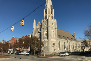 Kirche St. Marien, eine große Kirche mit einem Turm, umgeben von Gebäuden, Straßenlaternen, Verkehrszeichen, Kraftfahrzeugen, Schildern und Bäumen unter einem klaren blauen Himmel.