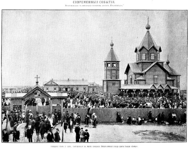 Schwarzer und weißer Schnappschuss einer Menge vor der Kirche der Interzession an der Nerl mit einem hölzernen Zaun im Vordergrund und Gebäuden im Hintergrund.