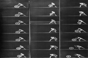 Ein Schwarz-Weiß-Foto eines Mannes im Rollstuhl, der ein Rad hält, ein weißes Hemd und dunkle Hosen trägt und einen entschlossenen Ausdruck hat.