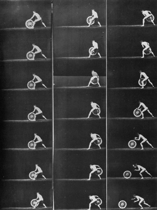 Ein Schwarz-Weiß-Foto eines Mannes im Rollstuhl, der ein Rad hält, ein weißes Hemd und dunkle Hosen trägt und einen entschlossenen Ausdruck hat.