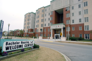 Ein Willkommenszentrum für Bachelor-Wohnungen mit Gebäuden, Straßeninfrastruktur, Fahrzeugen, Grünflächen und einem klaren Himmel.