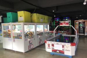 Ein Raum voller verschiedener Arcade-Spiele, mit einem Spielautomaten auf der rechten Seite, einem sichtbaren Boden und Deckenleuchten.