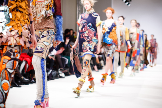 Eine Gruppe Von Frauen, Die Auf Einem Laufsteg In London Fashion Week Gehen, Mit Sitzenden Zuschauern Und Bühnenbeleuchtung Im Hintergrund.