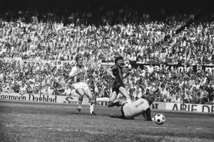 Schwarzes und weißes Foto von MГ¤nnern, die auf einem Feld Fussball spielen, mit Zuschauern im Hintergrund und einer Bundesliga 1978-79 Ajax 1-1 Hannover 96 Fahne.