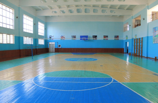 Großes Gymnastikgerät mit blauen und weißen Boden, Basketballfeld, Netz, Stützpfosten, Tür, Fenstern, Wandplakaten, Geländer und Dachkonstruktion.