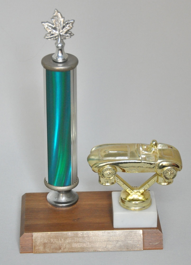 Ein glänzender, detailreicher Pokal mit einem Miniaturauto darauf, auf einer hellen Holzplatte montiert.