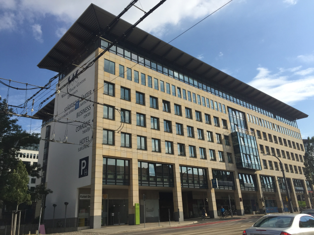 Großes modernes Gebäude mit zahlreichen Fenstern, als Stadthalle Center for Business bezeichnet, umgeben von Bäumen und städtischer Infrastruktur in Köln, Deutschland.
