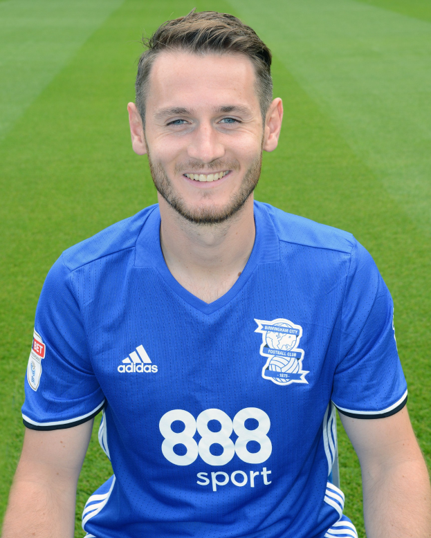 Ein Mann in einem blauen T-Shirt sitzt auf einem Fußballfeld während eines Trainings, lächeln.