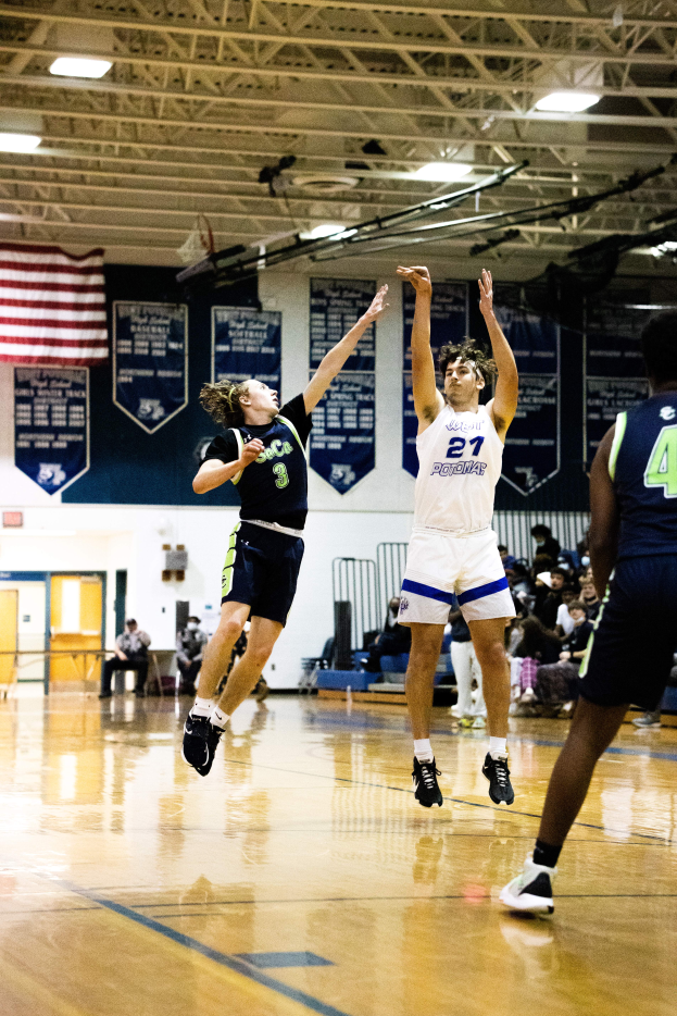 Eine Gruppe von Menschen, die Basketball in einer Turnhalle spielen, mit Zuschauern im Hintergrund, Bannern und einer Flagge an der Wand und einer Decke mit Stangen und Lampen darüber.