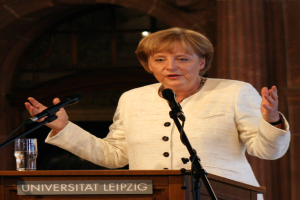 Bundeskanzlerin Angela Merkel hält eine Rede an der Universität Leipzig und steht hinter einem Rednerpult mit einem Mikrofon und einem Glas Wasser.