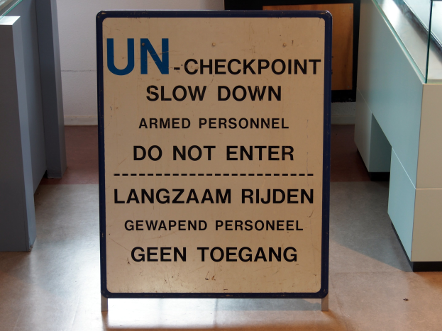 Bodenaufschrift "UN-Checkpoint Slow Down Armed Personnel - Do Not Enter" mit einer Glasplatte und Gegenständen rechts und einer Wand mit einem Gegenstand im Hintergrund.