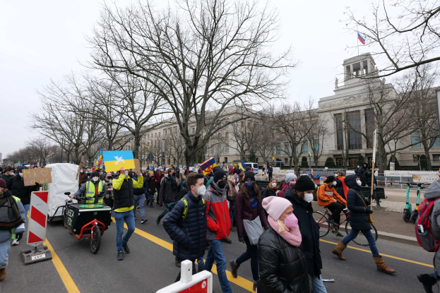 Eine große Gruppe von Menschen marschiert auf einer Straße in Washington, D.C. am 21. Januar 2020, einige halten Schilder und Banner, andere fahren Fahrräder, mit Bäumen und einem klaren blauen Himmel im Hintergrund.