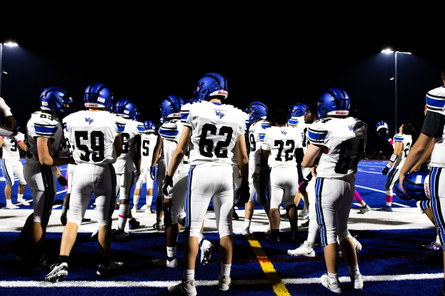 Eine Gruppe von Fussballspielern in Helmen und Stutzen, die auf einem Feld unter Flutlicht stehen und bereit zum Spiel zu sein scheinen.
