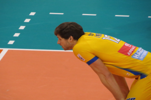 Eine professionelle Volleyballspielerin in einem gelben "Volleyball"-T-Shirt steht selbstbewusst auf einem Court und bereitet sich auf den Aufschlag vor.