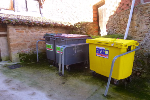 Zwei gelbe und graue Mülltonnen mit Rollen nebeneinander vor einem Gebäude mit Wand und Fenster im Hintergrund.