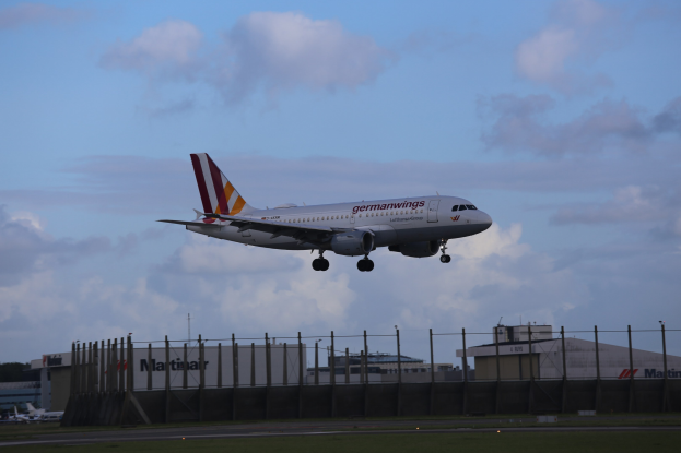 Germanwings Airbus A320-200 beim Starten am Frankfurter Flughafen mit Gras, einem Zaun, Gebäuden, Bäumen und einem bewölkten Himmel im Hintergrund.