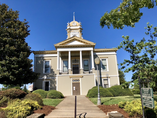 Großes Backsteingebäude mit einem Uhrenturm, mehreren Fenstern, Türen und Säulen, als altes Rathaus bezeichnet, umgeben von Straßenlaternen, einem Schild, Bäumen, Gras und einem bewölkten Himmel.
