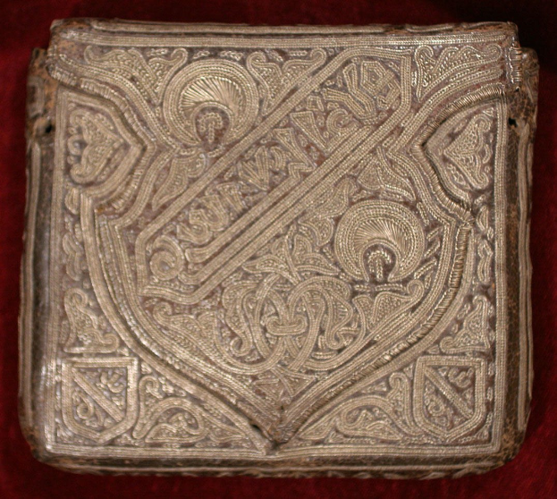 Ein goldbedecktes altes Buch mit detaillierten Designs auf einem roten Samtgrund.