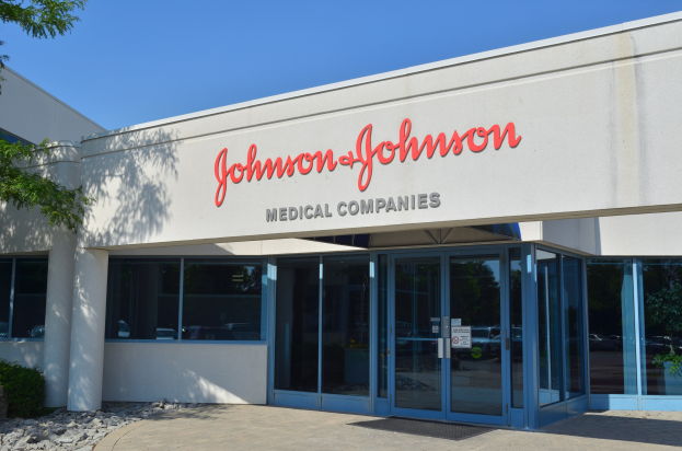 Außenansicht des Johnson & Johnson Medical Companies-Gebäudes mit Glaswänden, Text an der Fassade, Steinen, Pflanzen und einem Baum auf der linken Seite unter einem klaren blauen Himmel.