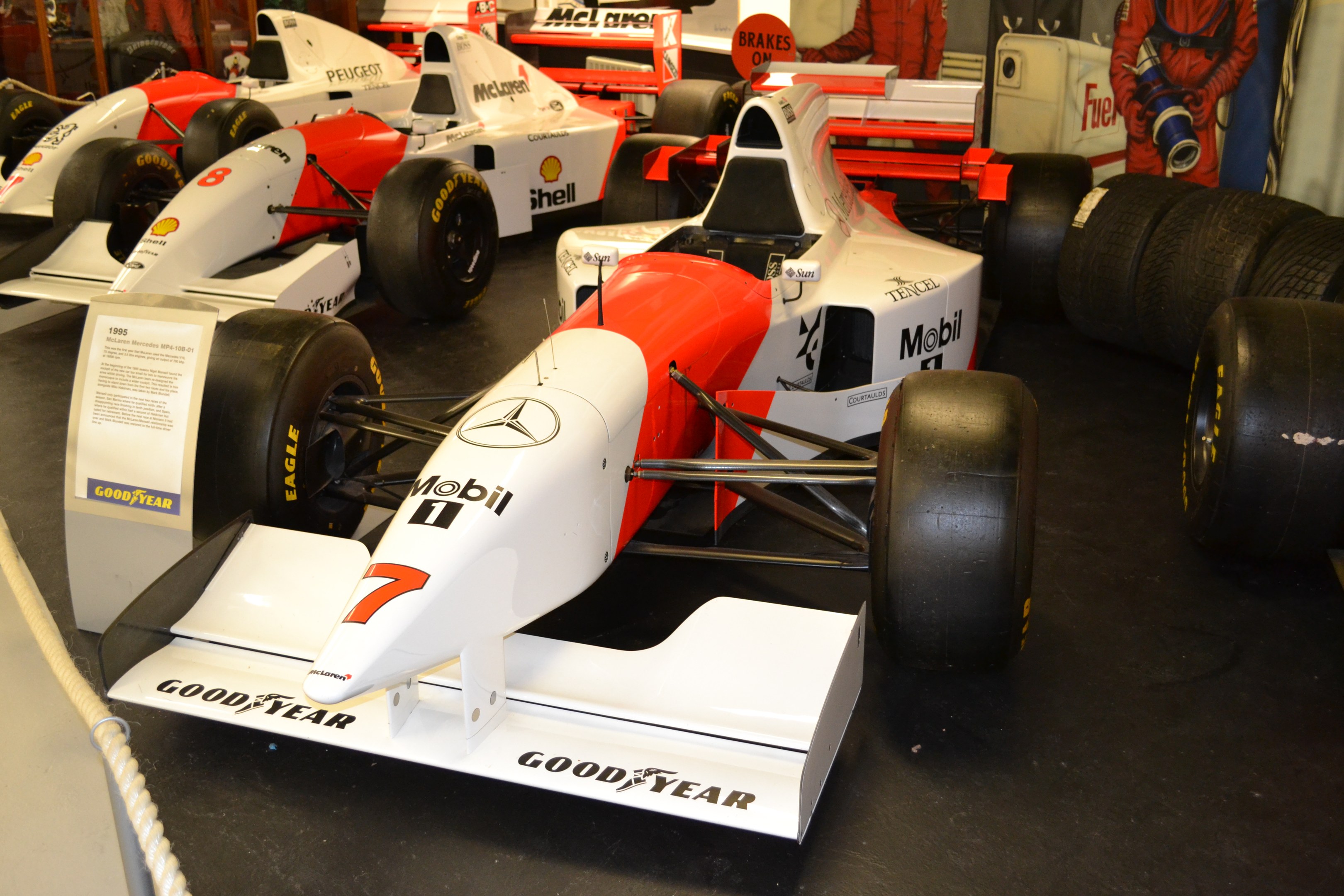 Eine Ausstellung von Rennwagen in einem Museum, mit Besuchern und Informationsschildern.