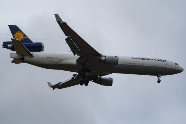 Ein Lufthansa Cargo Boeing 777-300ER im Flug, mit ausgefahrenen Tragflächen und aktivierten Triebwerken, mit sichtbarem Text auf dem Rumpf und weißen Wolken am Himmel.