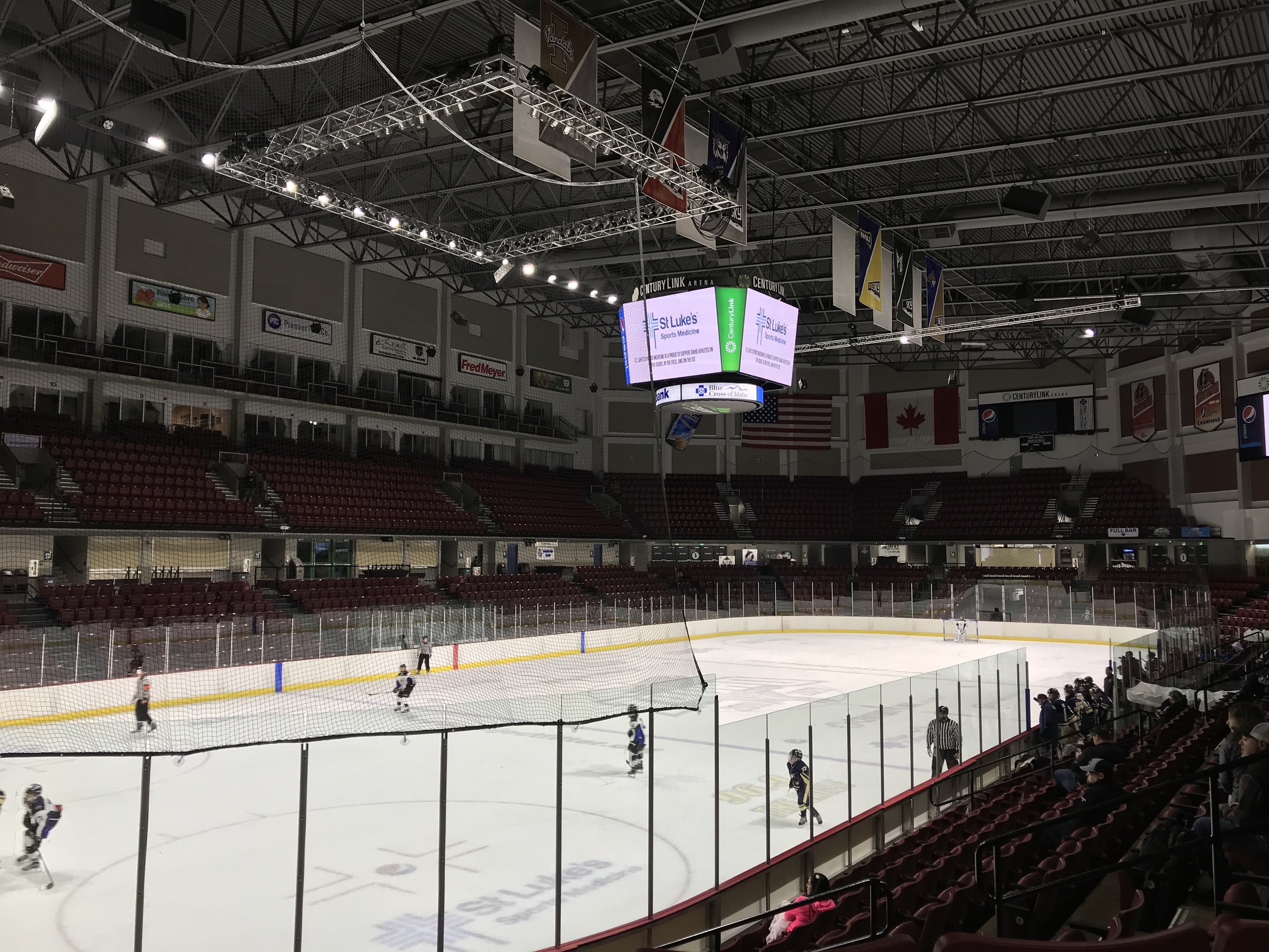 Eishockeyspiel in einer großen Arena mit einem zentralen Netz, Zuschauern auf Stühlen, Deckenbeleuchtung und Bannern, identifiziert als die St. Louis Blues Arena.