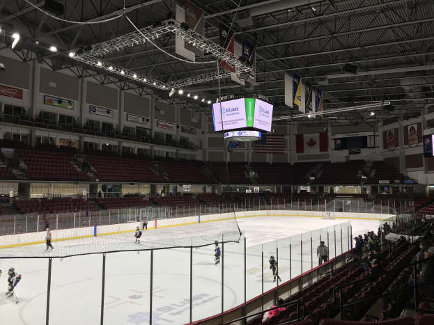 Eishockeyspiel in einer großen Arena mit einem zentralen Netz, Zuschauern auf Stühlen, Deckenbeleuchtung und Bannern, identifiziert als die St. Louis Blues Arena.